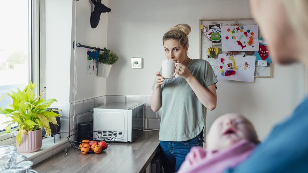 Mutter trinkt Tee, während die Oma das Baby hält.