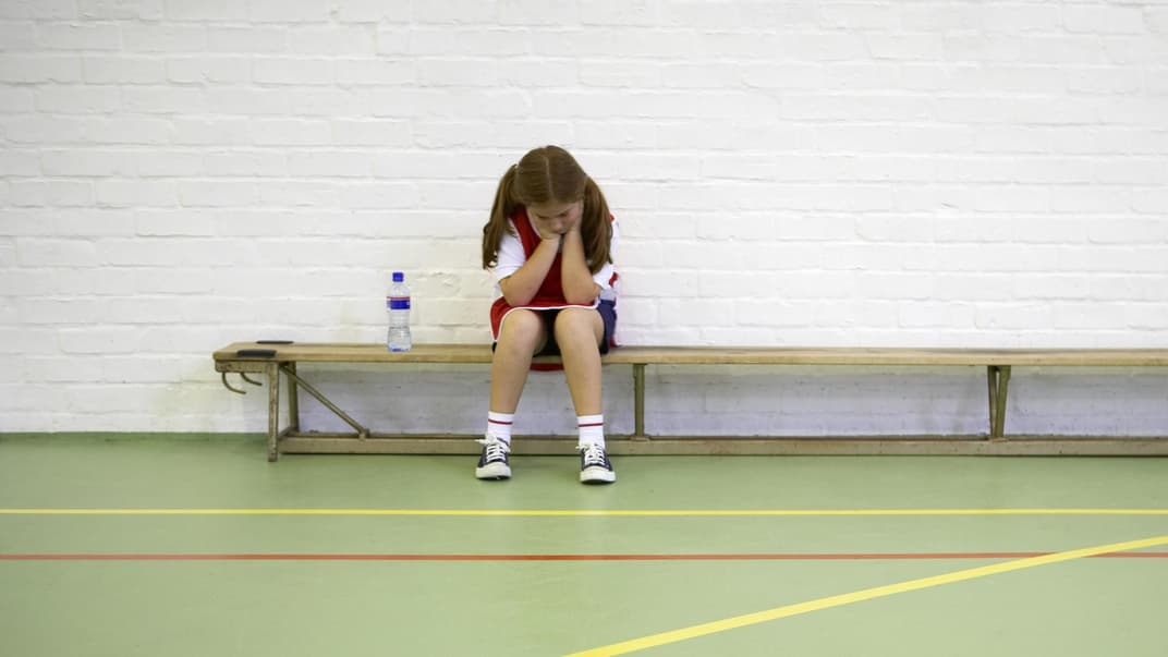 Ein Mädchen sitzt beim Schulsport frustriert auf der Bank. 