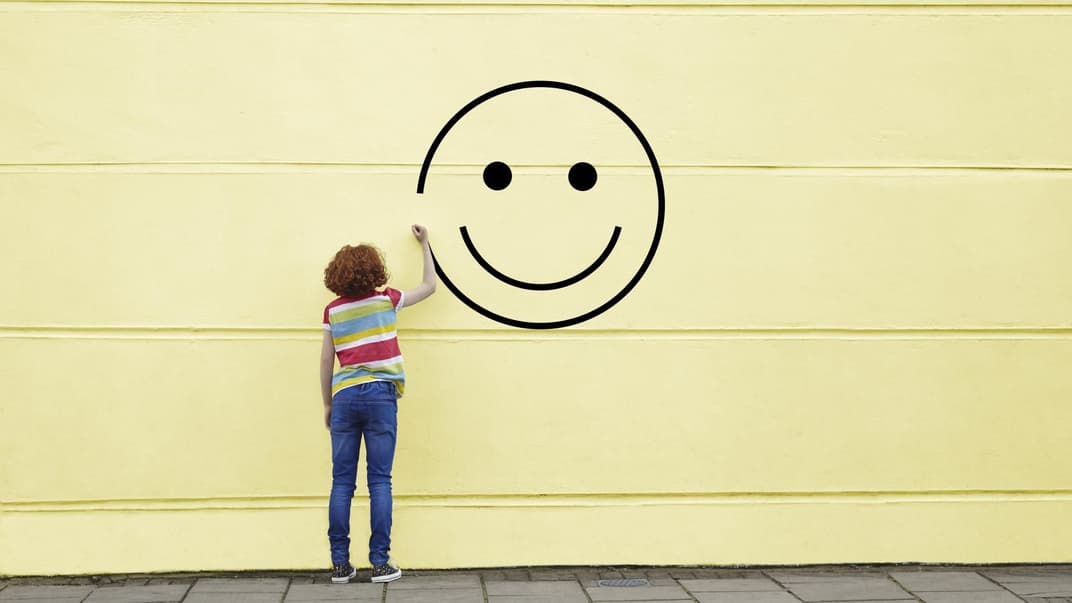 Mädchen malt Smiley an gelbe Wand.