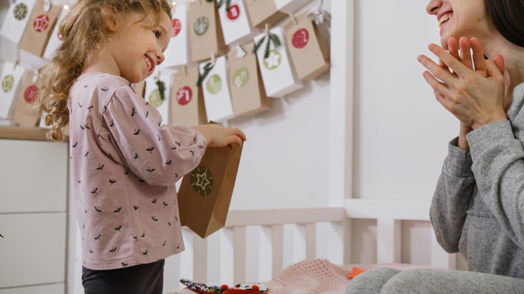 Kleines Mädchen öffnet ihren Montessori-Adventskalender. Und Mama freut sich mit!