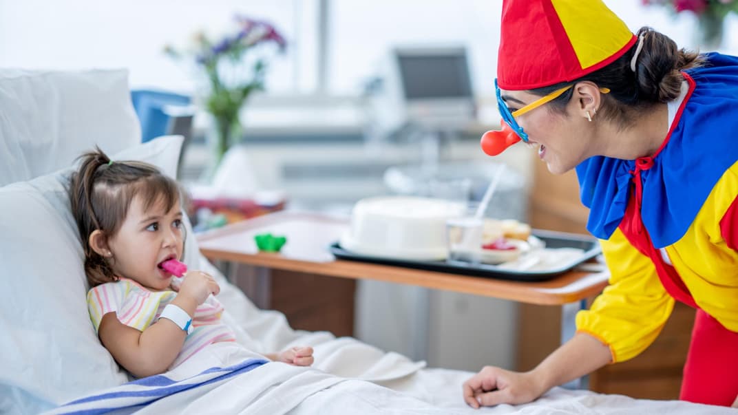 Ein weiblicher Klinik-Clown überrascht ein kleines Mädchen im Krankenhaus.