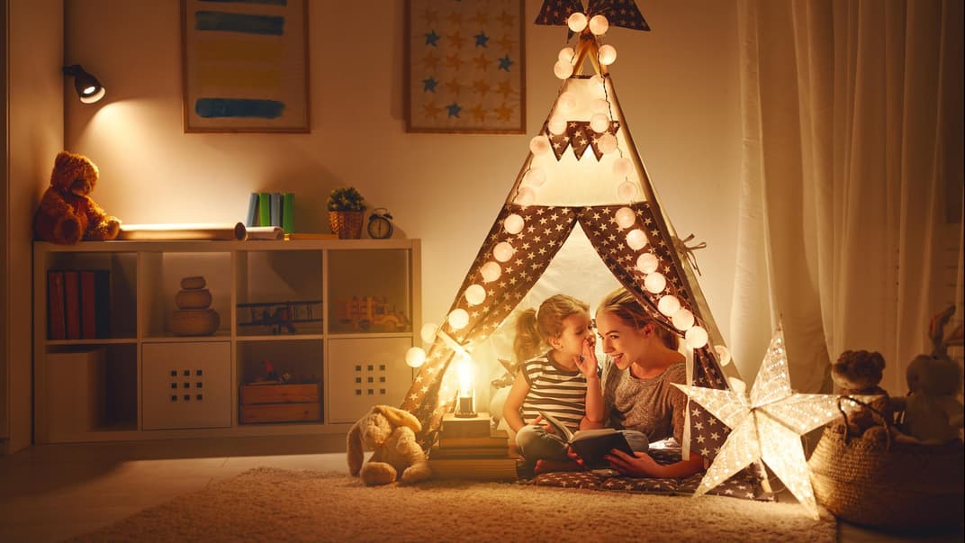 Tochter und Mutter sitzen im Tipi im aufgeräumten Kinderzimmer bei gemütlichem Licht.