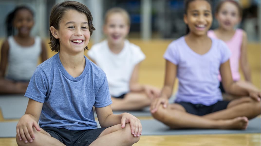 Fröhliche Kinder sitzen in der Schule auf Yogamatten.