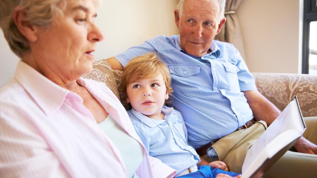 Oma und Opa lesen mit dem Enkel ein Buch. 