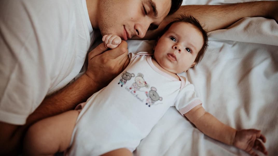 Papa hält beim Schlafen die Hand seines Babys. 