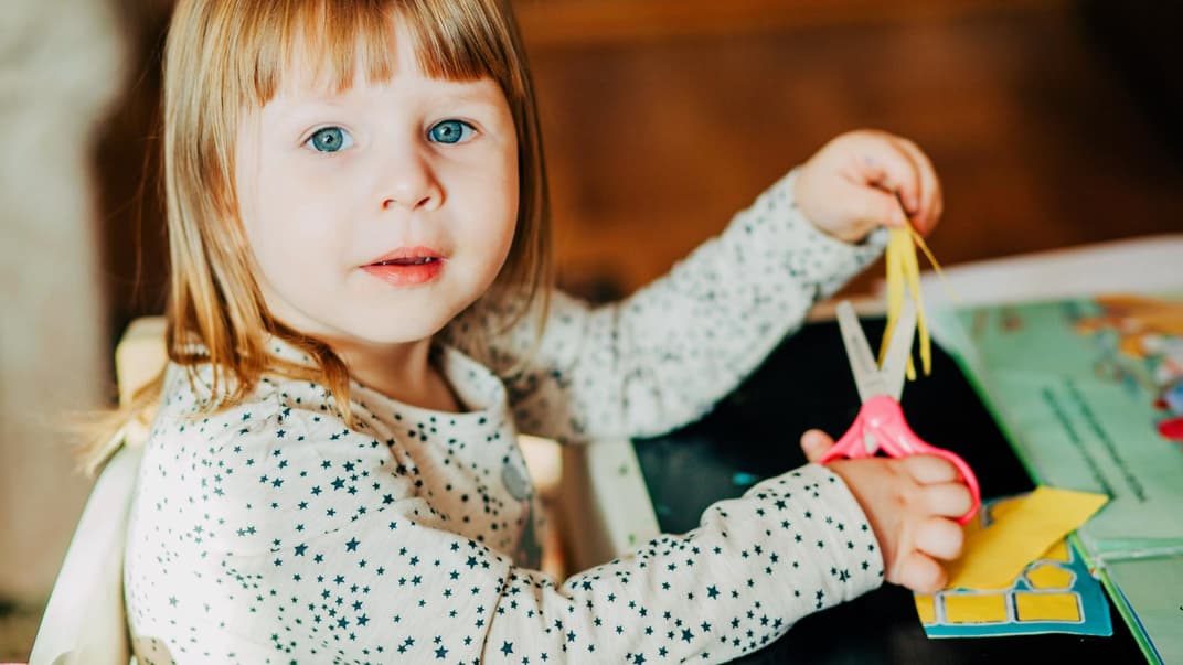 Kleines Mädchen übt mit der Schere das Schneiden