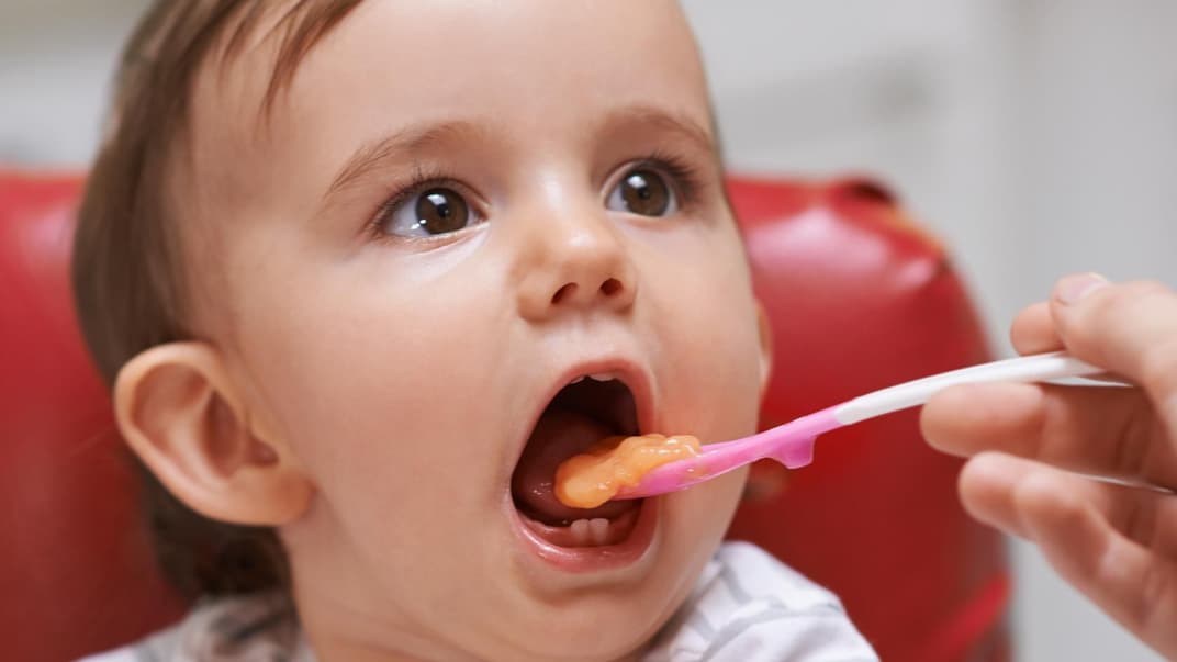 Ein kleines Kind isst einen Löffel Brei aus einem Babygläschen. 