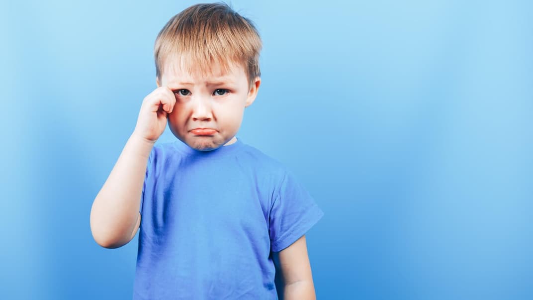 Kleiner Junge mit Schmollmund, reibt sich das Auge.