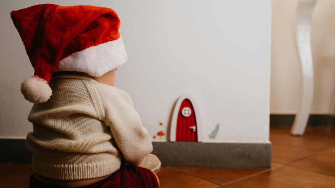 Baby-Junge mit Weihnachtsmütze sitzt vor der weihnachtlichen Wichteltür