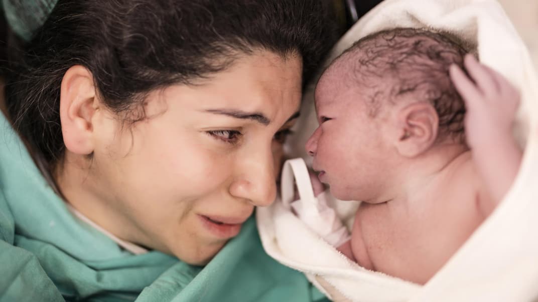 Eine frisch gebackene Mutter weint als sie ihr Baby endlich neben sich liegen hat.