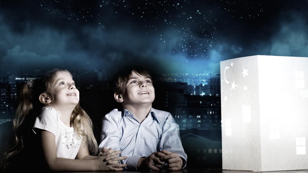 Ein Junge und ein Mädchen starren begeistert in den projizierten Sternenhimmel im Zimmer.