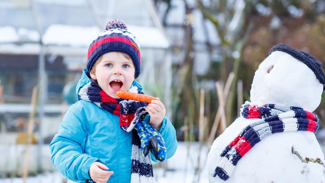 Kind beißt in die Möhre des Schneemanns.