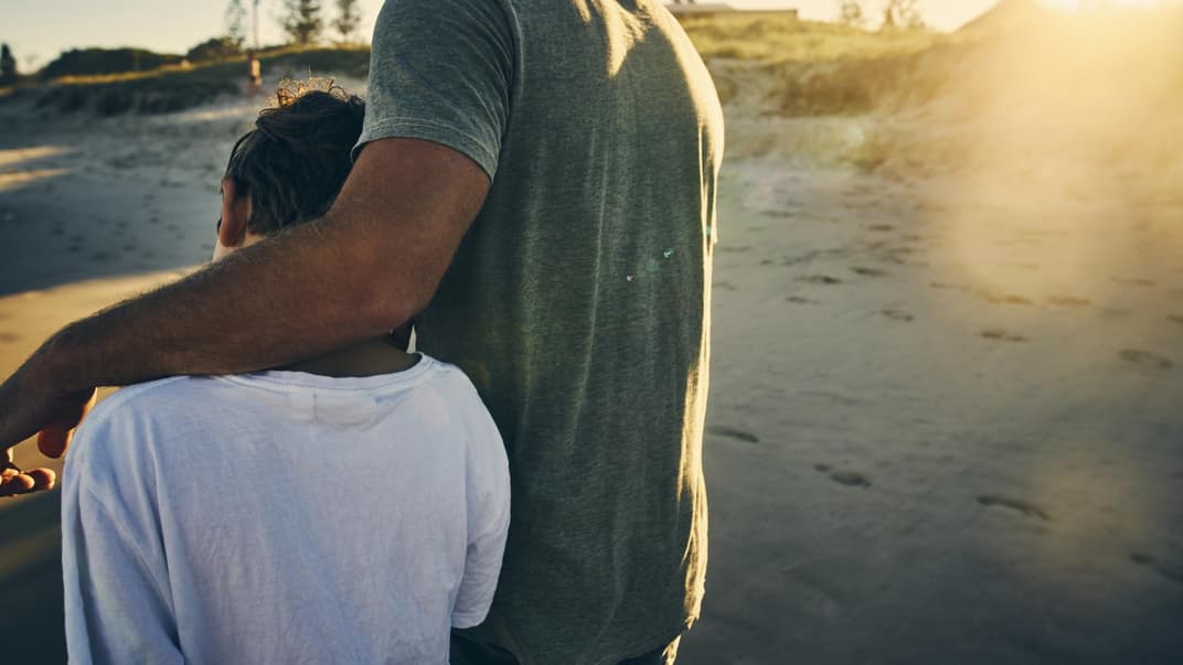 Vater legt den Arm um seinen Sohn am Strand.