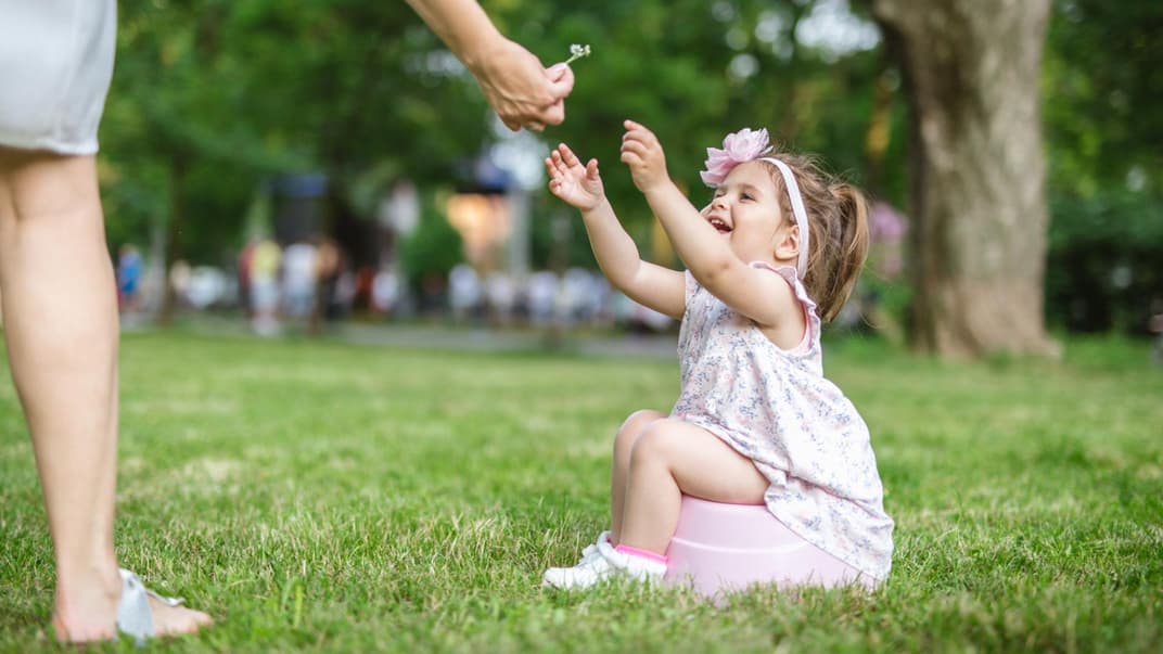 Ein kleines Mädchen sitzt im Park auf einem Reisetöpfchen.