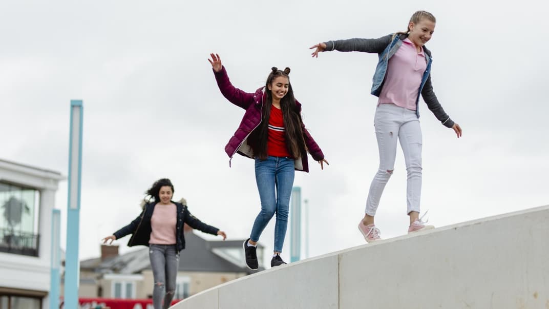 Jugendliche Mädchen balancieren auf hoher Mauer.