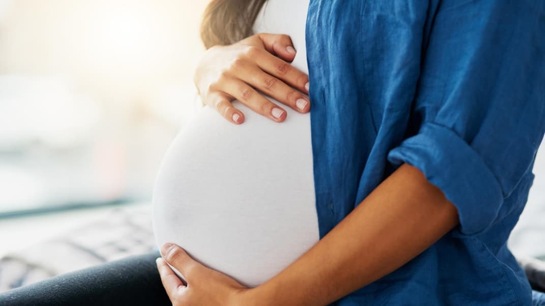 Schwangere Frau hält ihren Babybauch in den Händen. 