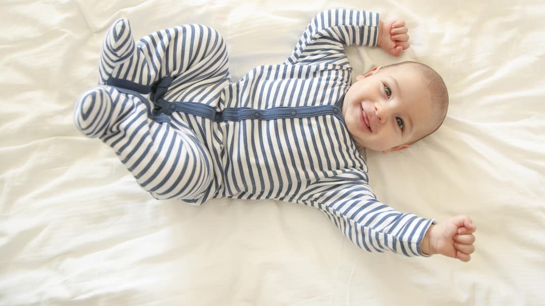 Baby-Junge in einem Strampler hat gute Laune und lacht.