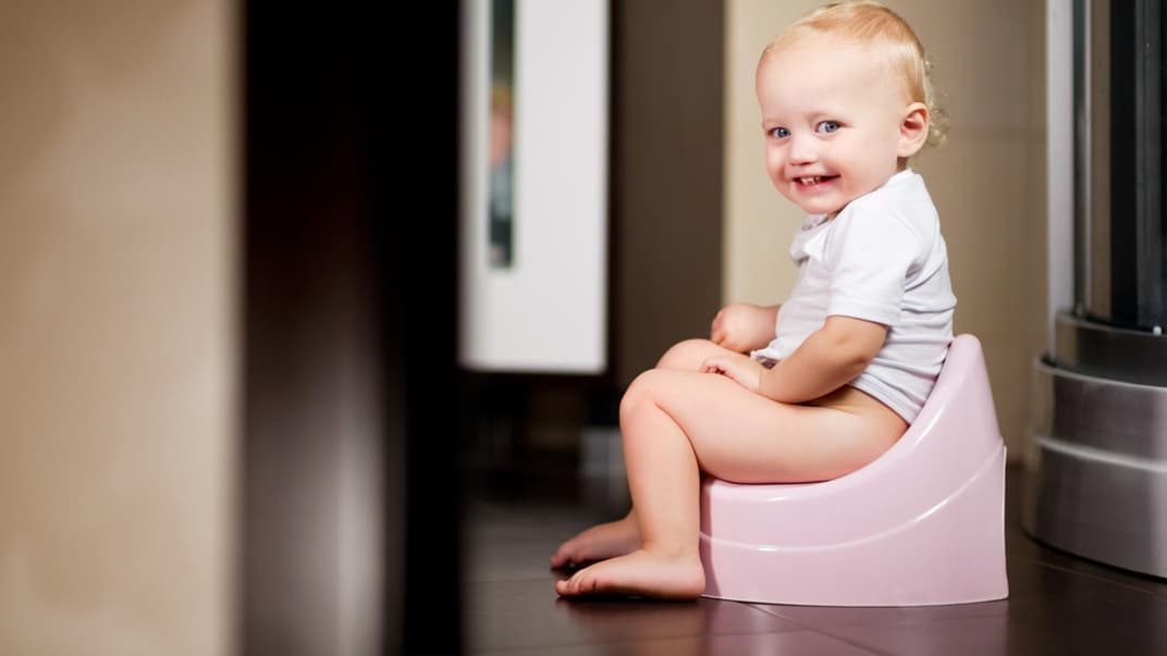 Kleines Mädchen sitzt auf einem Topf im Badezimmer und lächelt.