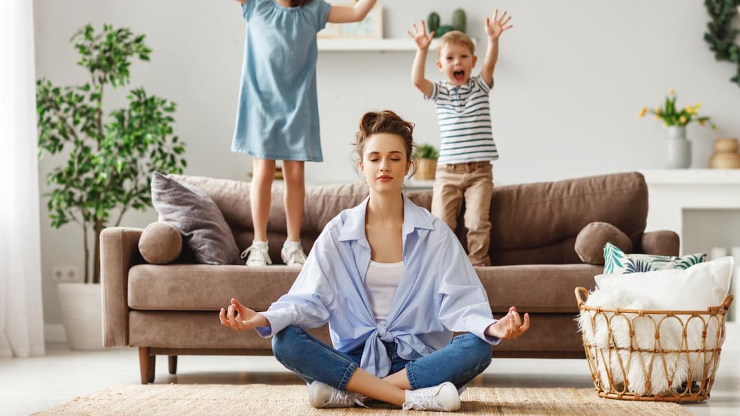 Kinder springen auf dem Sofa, Mutter meditiert.
