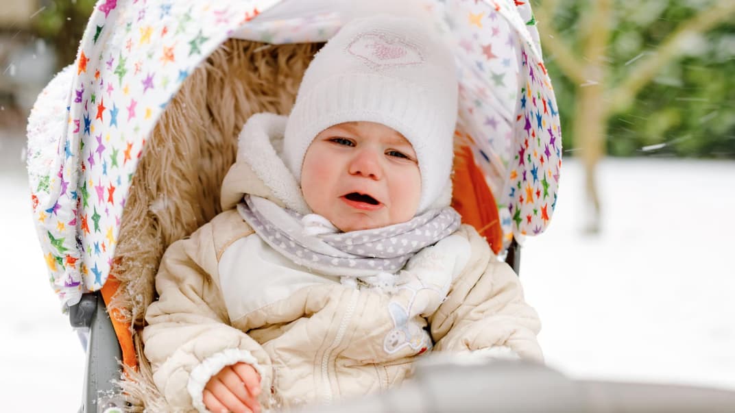 Ein Kleinkind ohne Handschuhe weint im Buggy im Winter.