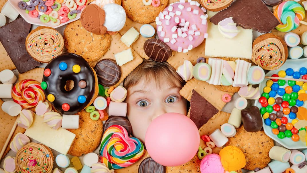 Kleines Kind, das unter vielen süßen Speisen liegt.