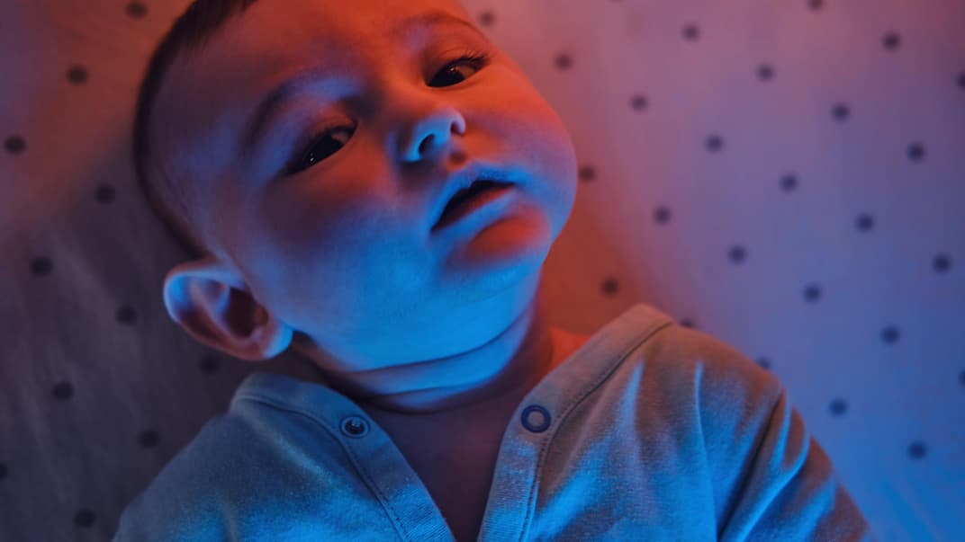 Baby-Junge liegt im Bettchen, im Licht einer Rotlichtlampe.