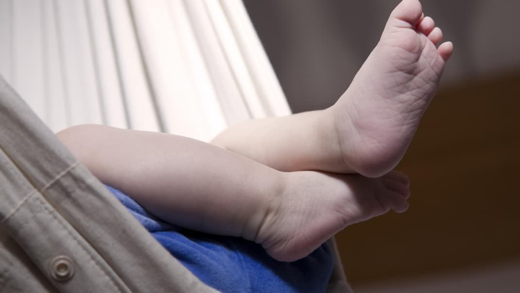 Viele Babys kommen in der Federwiege gut zur Ruhe. Babyfuß ragt aus der Federwiege.