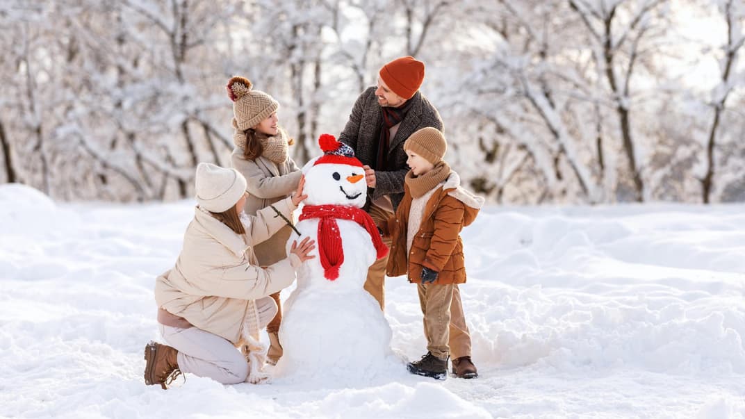 Eine vierköpfige Familie baut einen Schneemann.