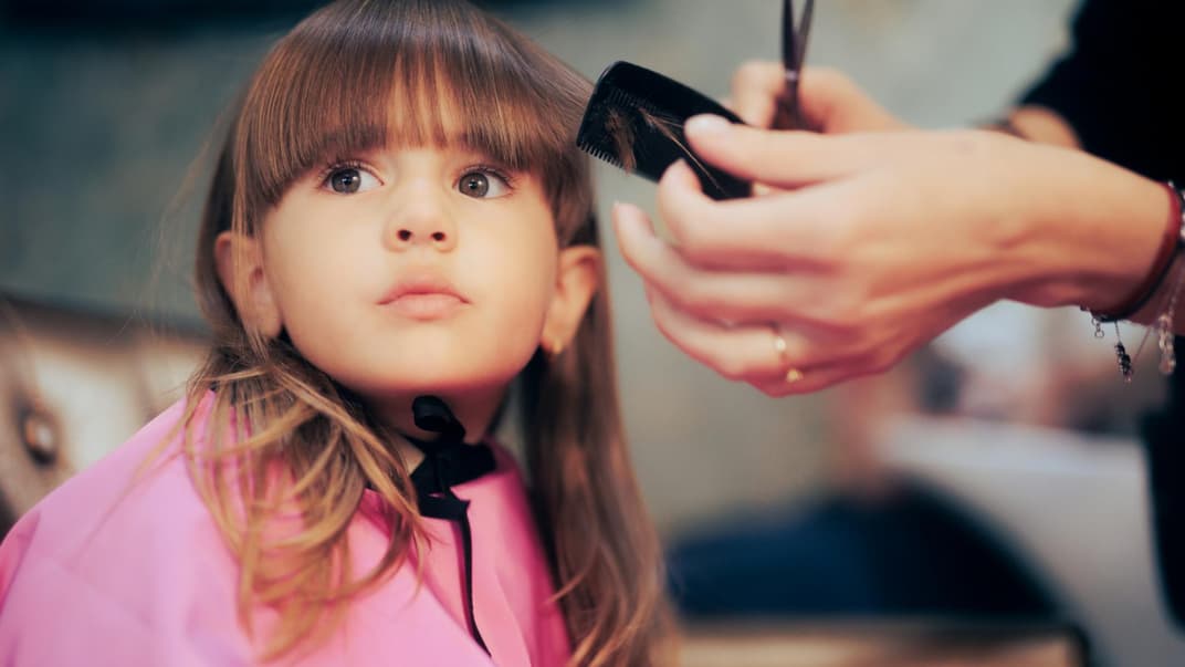 Einem kleinen Mädchen mit langen haaren wird der Pony geschnitten.