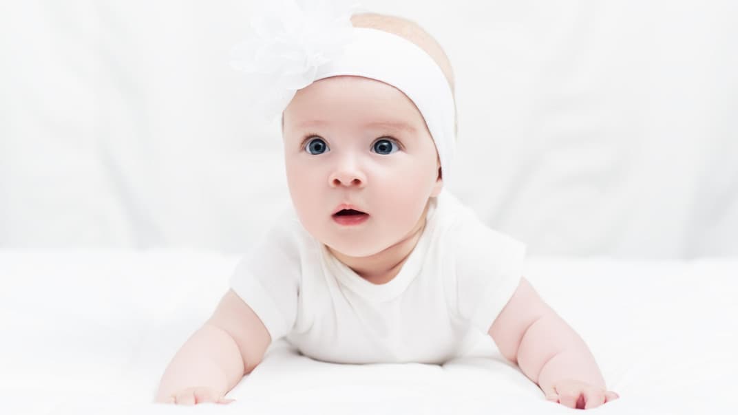 Baby in Bauchlage mit niedlichem Kopfband.