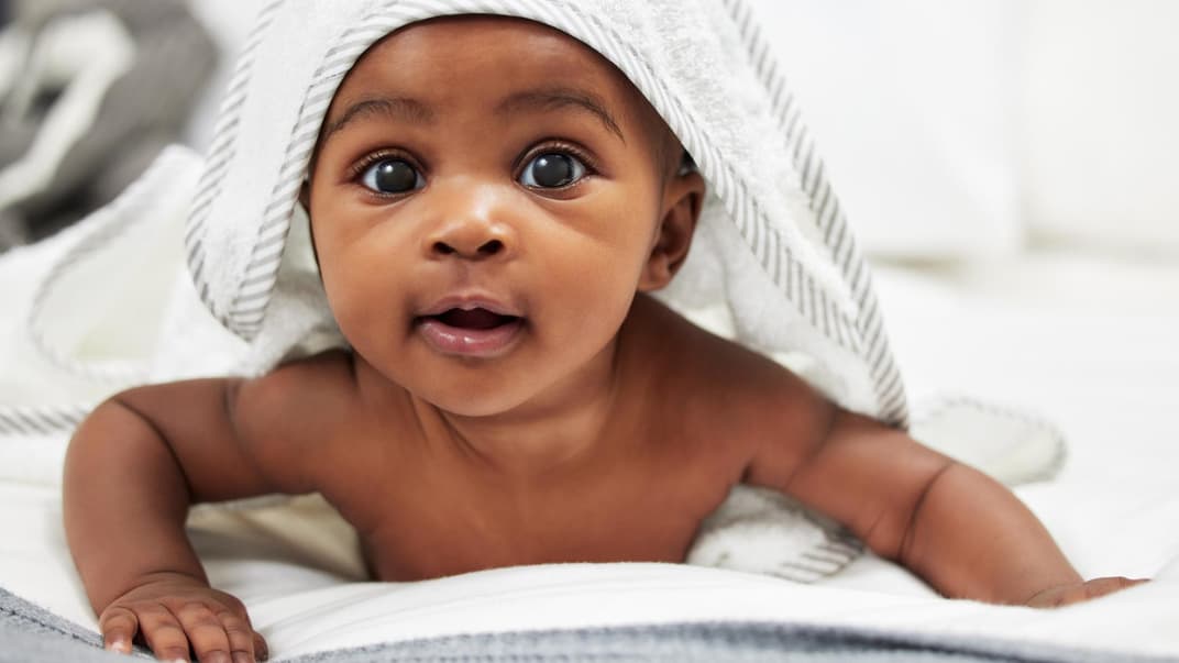 Niedliches, afrikanisches Baby unterm Kapuzenhandtuch.