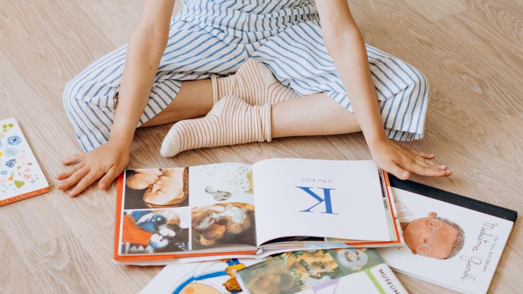 Ein Mädchen liest Bücher auf dem Boden. 