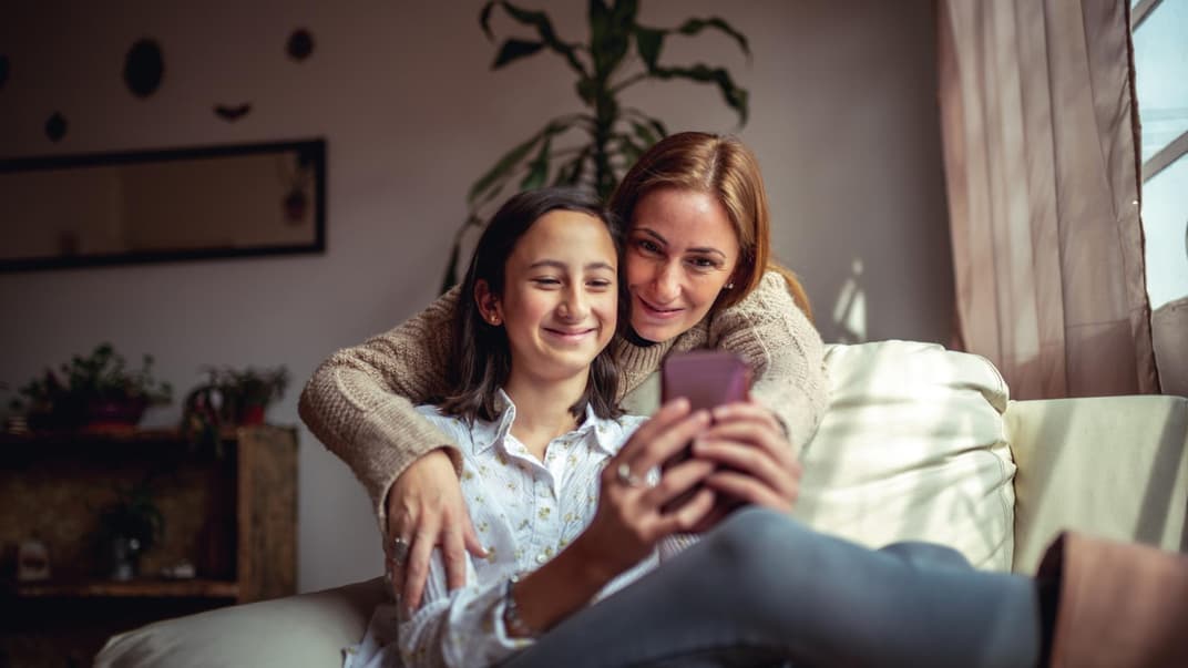 Mutter und Tochter mit Smartphone auf dem Sofa: Elektronikartikel für Kinder kann man auch gebraucht kaufen