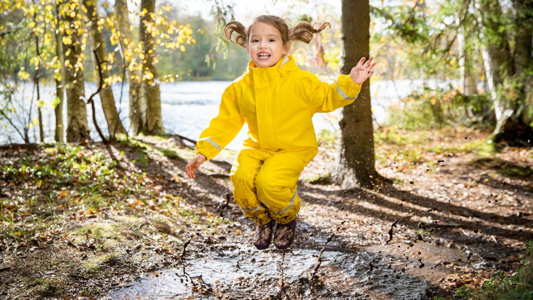Kind spielt draußen und springt in Pfütze
