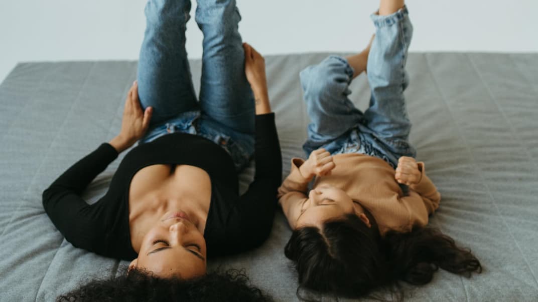 Mutter und Tochter liegen auf dem Rücken und strecken die Beine hoch.