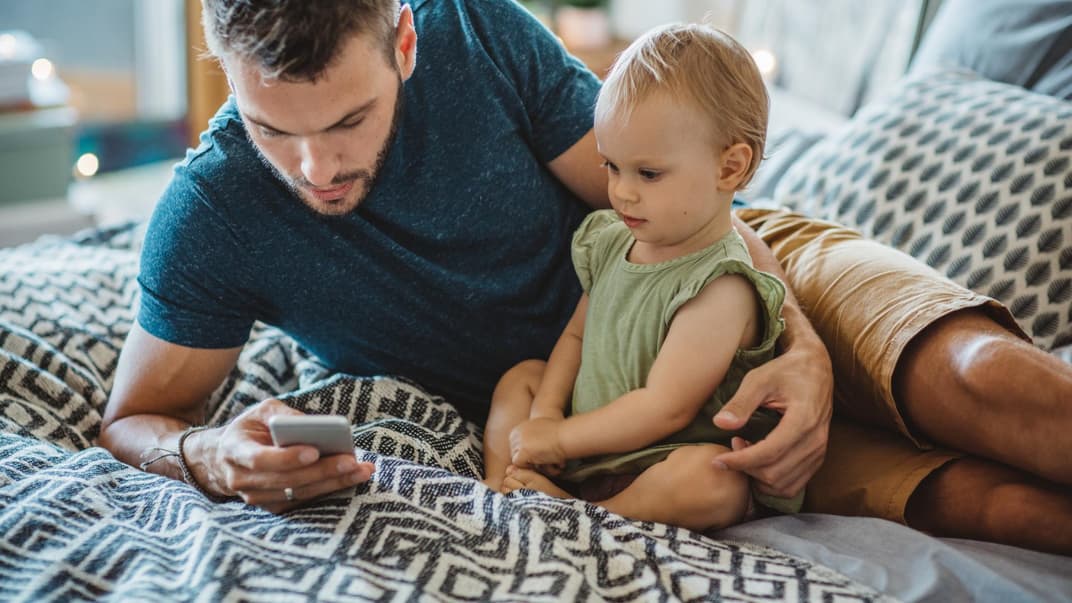 Vater sitzt neben seiner Tochter und guckt aufs Handy