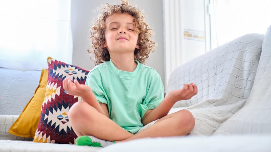 Kind sitzt auf dem Sofa und meditiert