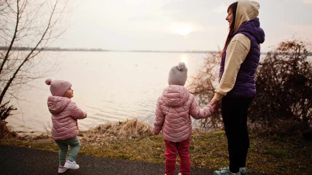 Mutter steht mit zwei kleinen Mädchen am See.