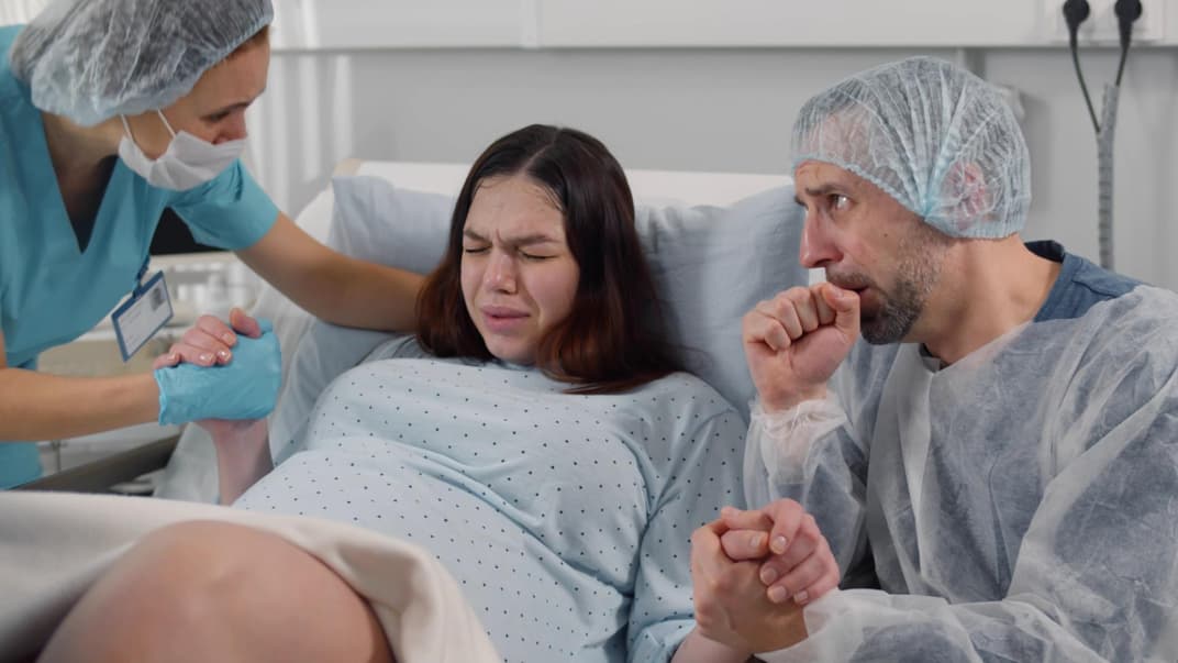 Verängstigter Ehemann, der im Kreißsaal die Hand einer Frau hält