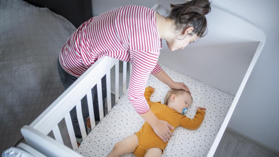 Mutter legt ihr schlafendes Baby ins Bett.