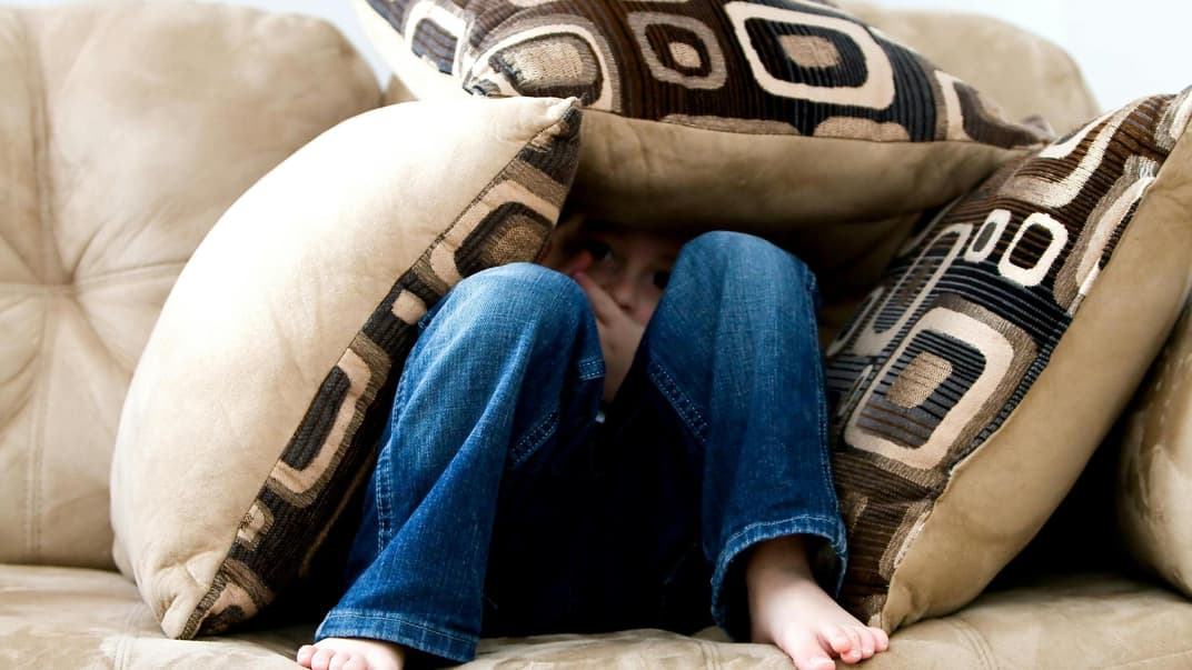 Kind versteckt sich unter Sofakissen.