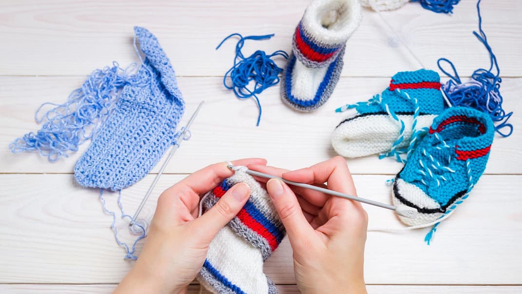 Eine Frau häkelt zwei Paar Kinderschühchen.