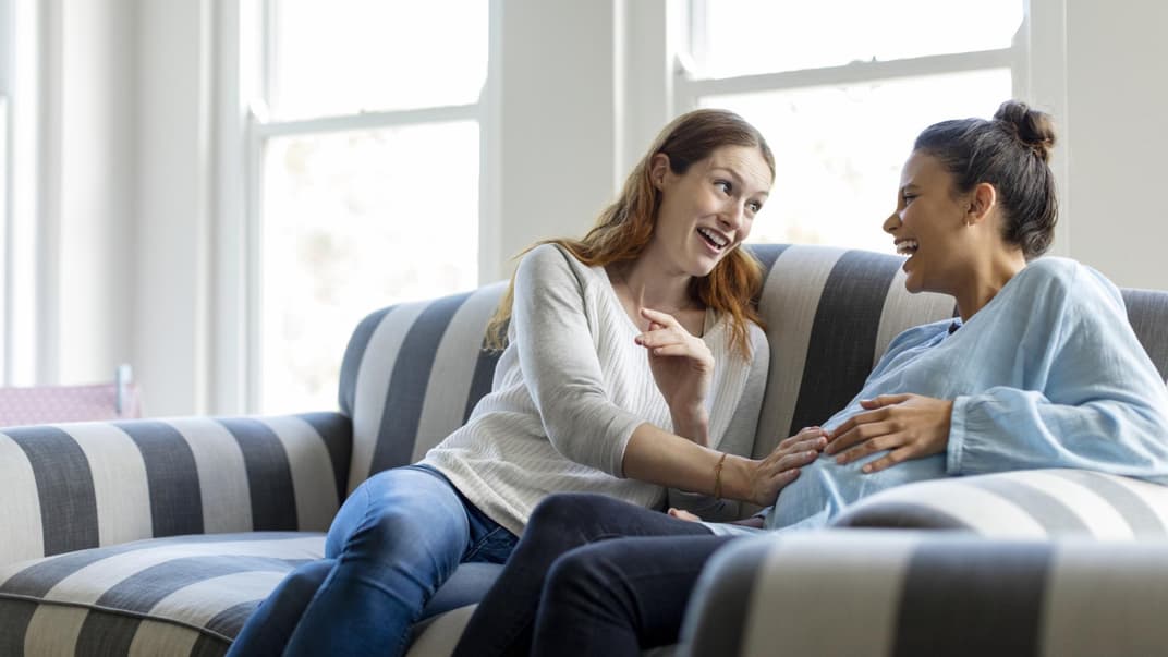 Frau legt ihrer schwangeren Freundin die Hand auf den Babybauch.