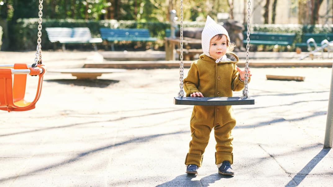 Ein Kleinkind im Wollwalkoverall auf dem Spielplatz