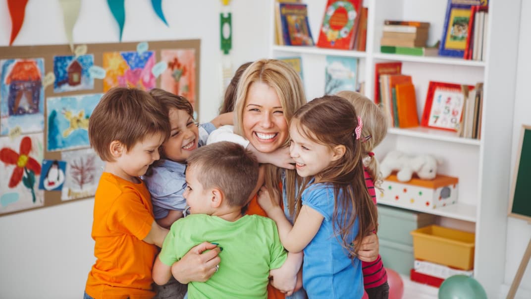 Eine Erzieherin wird herzlich von den Kindern zum Geburtstag umarmt.