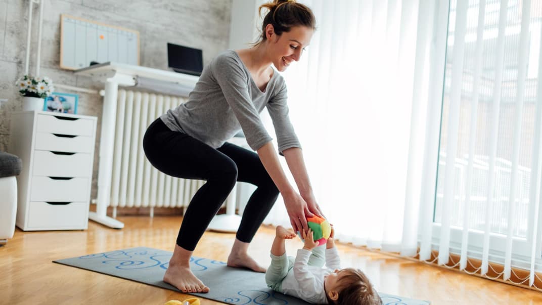 Eine Mutter trainiert ihren Beckenboden, während ihr Baby vor ihr liegt.