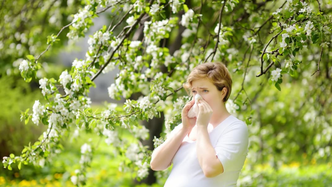 Eine schwangere Frau putzt sich auf einer Wiese die Nase. 