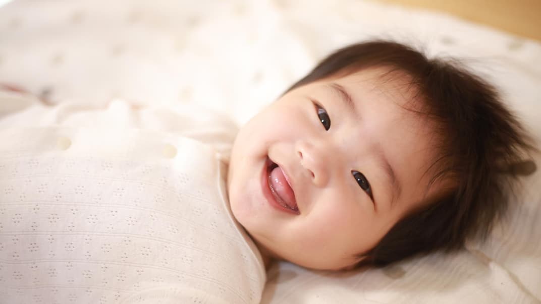 Japanisches Baby liegt lachend im Bett.