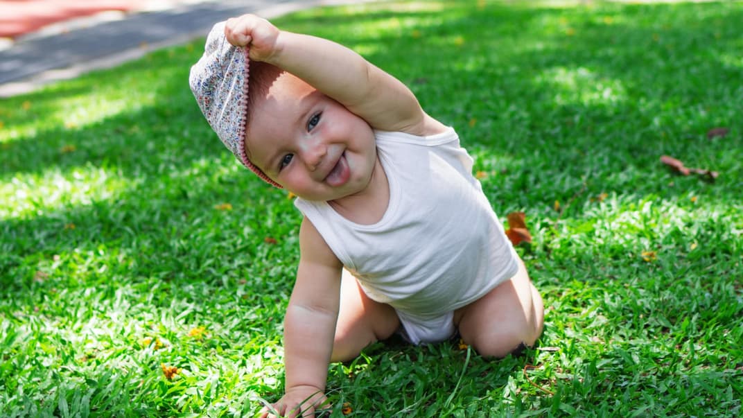 Schwitzen Babys im Sommer? Ein kleines Baby, das sich die Mütze vom Kopf zieht.