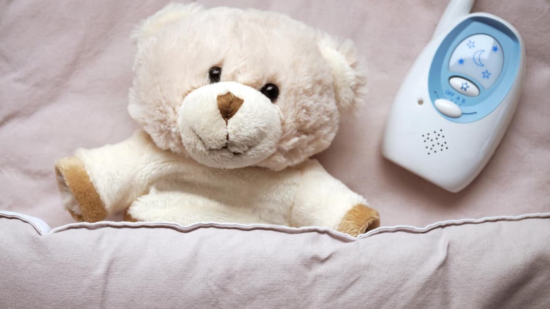 Ein Teddy liegt neben einem Babyphone. 